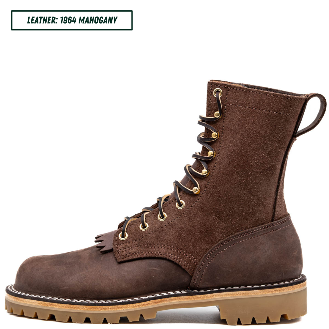 A single brown suede lace-up boot shown in side profile on a white background, with a text label in the top-left corner reading 'LEATHER: 1964 MAHOGANY'. The boot has dark brown laces, brass eyelets, a pull loop, and a tan lug sole with white stitching.