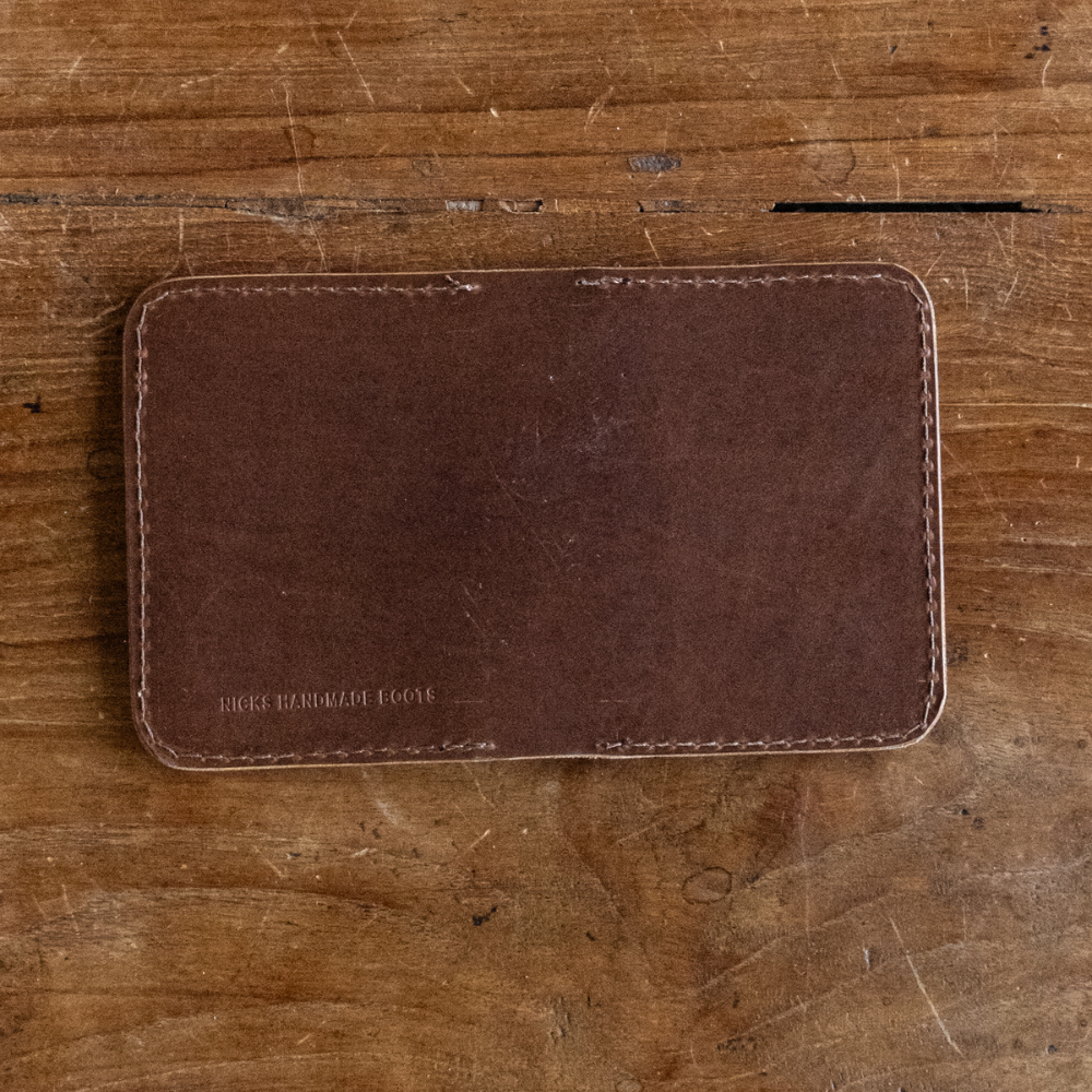 Dark brown leather Heritage Calf Wallet with stitched edges and stamped logo on a wooden background