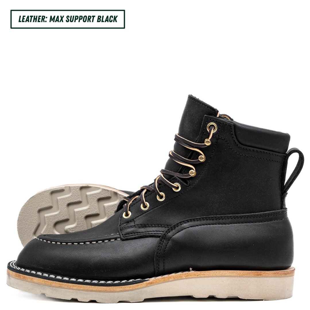 A black leather lace-up work boot shown in profile on a white background, with a second boot placed behind it to display the outsole. A small text label in the top left reads 'LEATHER: MAX SUPPORT BLACK'.