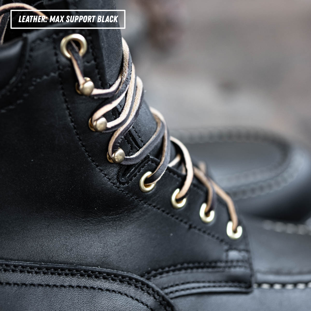 Close-up of a black leather lace-up boot with metallic gold eyelets and laces, featuring a text overlay that reads 'LEATHER- MAX SUPPORT BLACK'.