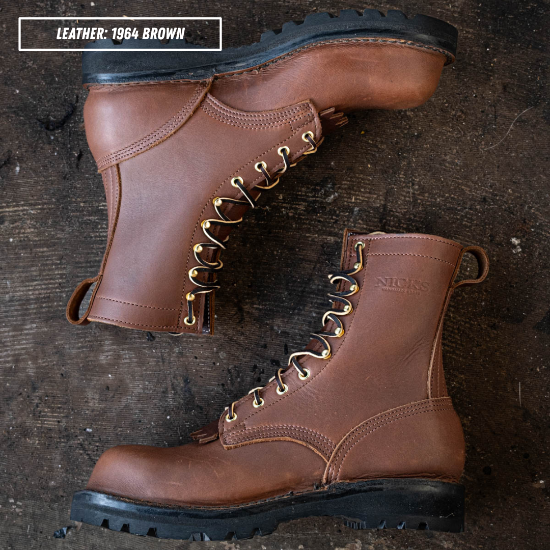 Two brown leather lace-up work boots arranged on a dark rustic wooden surface. One boot is positioned upright and the other lies on its side, showing the side profile and front three-quarter view.