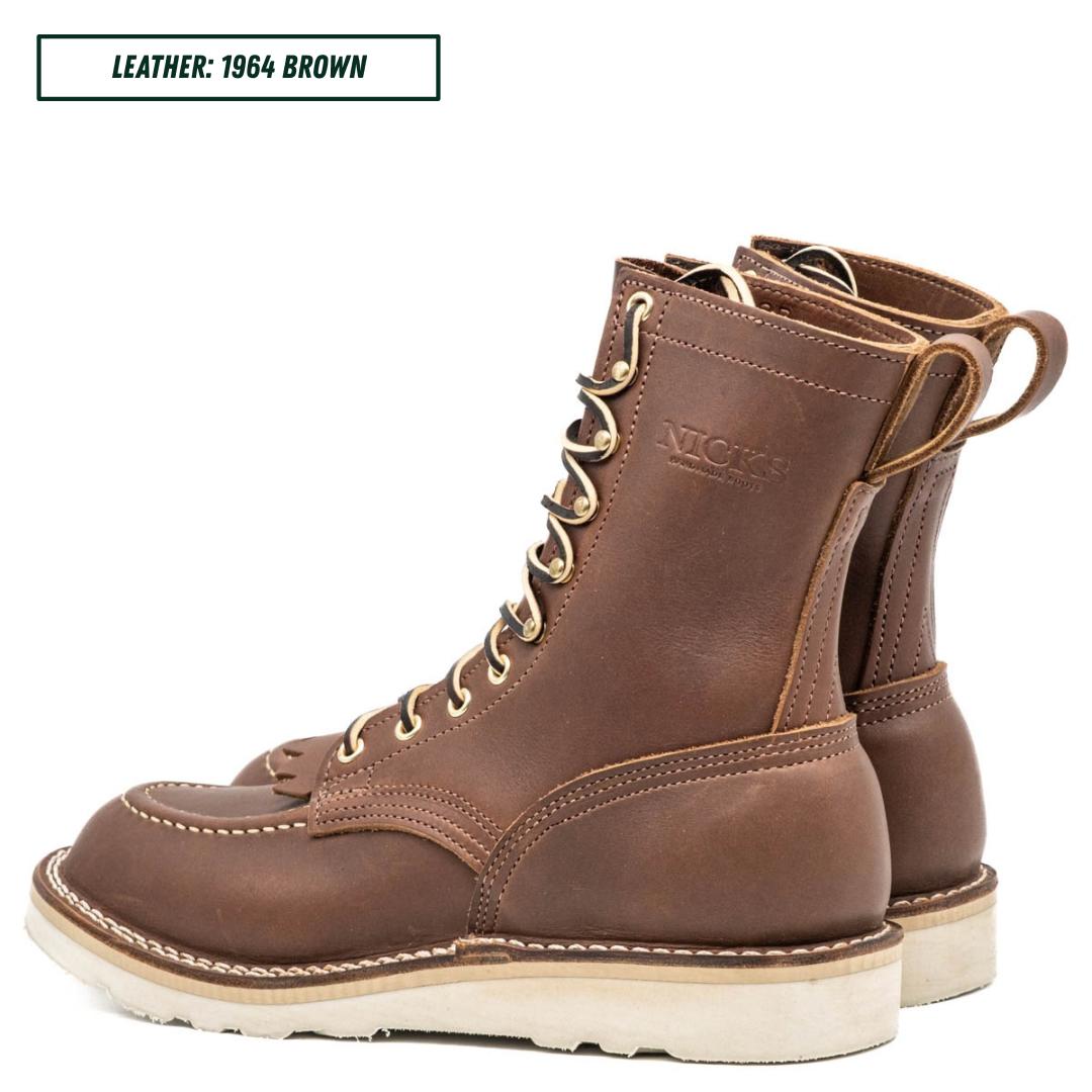 A pair of brown leather lace-up boots shown on a white background, with a text label in the top-left corner reading 'LEATHER: 1964 BROWN'. The boots feature a rich medium brown leather upper, brass eyelets, off-white stitching, and a thick off-white sole.