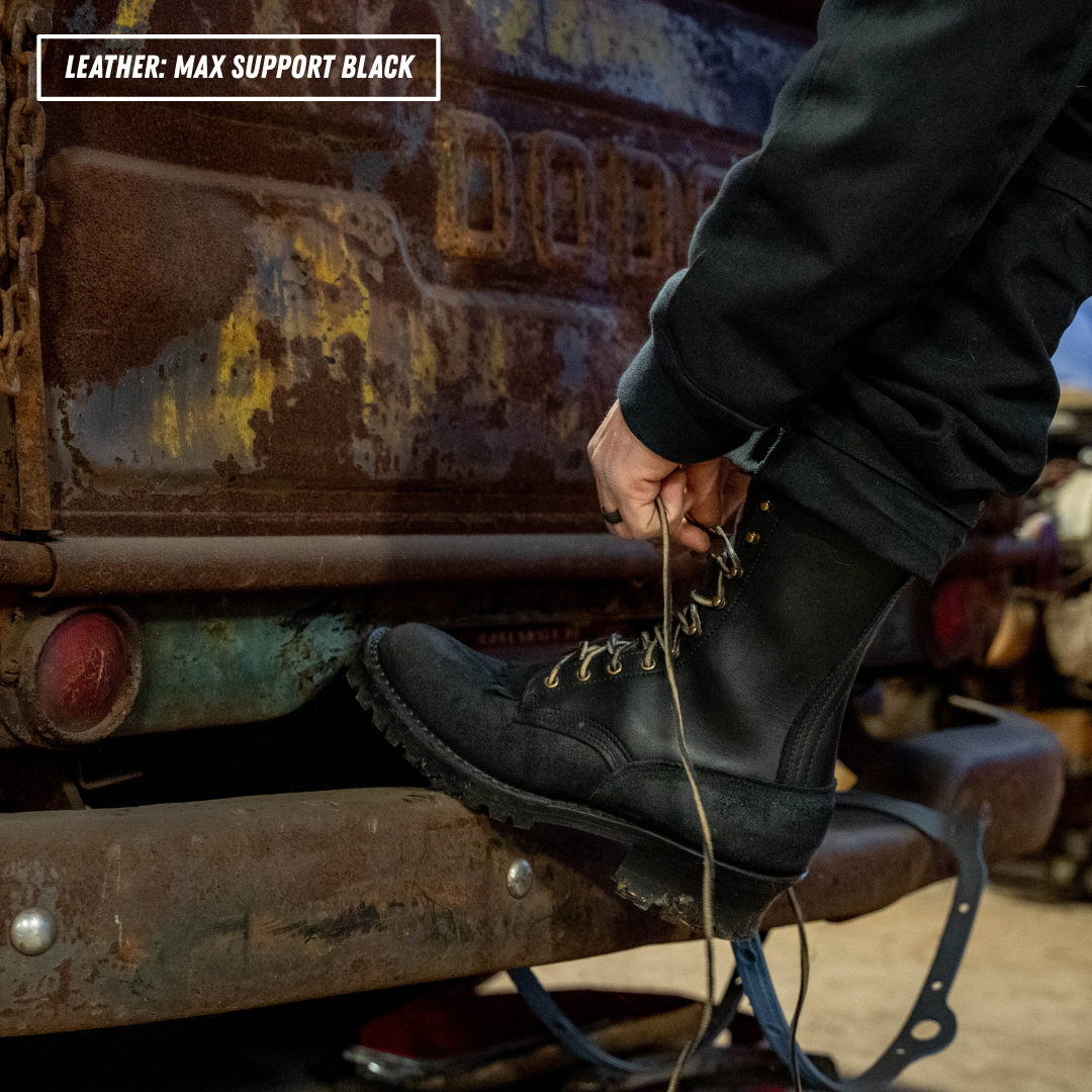 A person wearing a black leather lace-up boot with metal eyelets and laces, stepping onto a rusty metal surface next to a vehicle while tying the boot. A text overlay in the top-left corner reads 'LEATHER: MAX SUPPORT BLACK'.