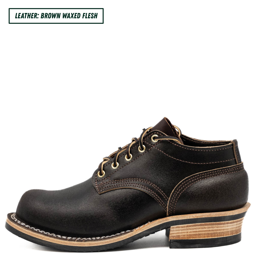 A single dark brown leather lace-up boot shown in side profile on a white background, with a text label in the top-left corner reading 'LEATHER: BROWN WAXED FLESH'. The boot has tan stitching, a stacked wood-look heel, and a black outsole.