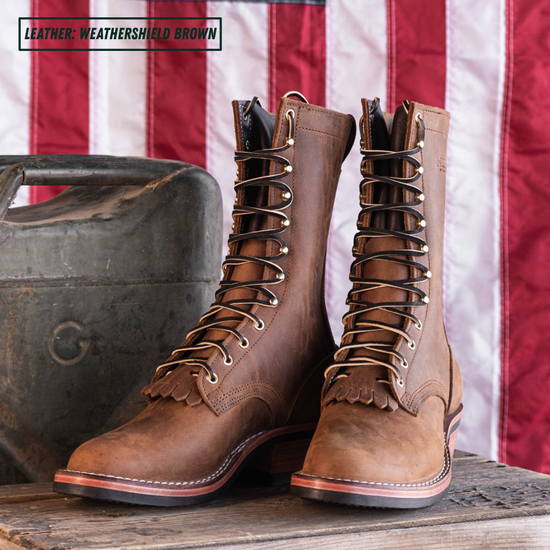 A pair of mid-calf lace-up boots in a weathered brown leather, styled on a rustic wooden surface with a vintage metal case and the American flag in the background. A text overlay in the top left reads 'LEATHER: WEATHERSHIELD BROWN'.