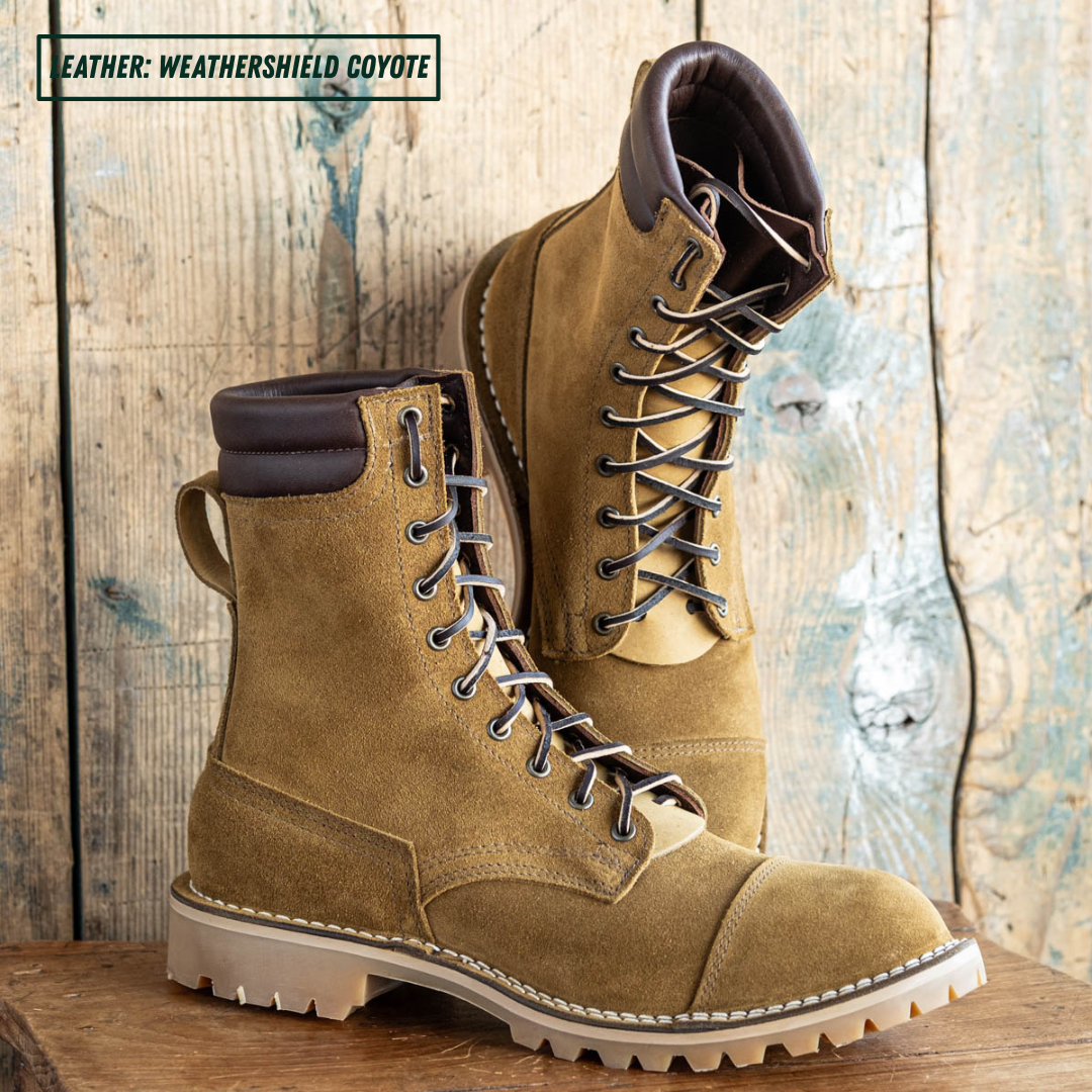 A pair of tan suede lace-up boots with dark brown trim and off-white lug soles, displayed on a rustic wooden surface against a weathered wood plank background. A text overlay in the top left reads 'LEATHER: WEATHERSHIELD COYOTE'.