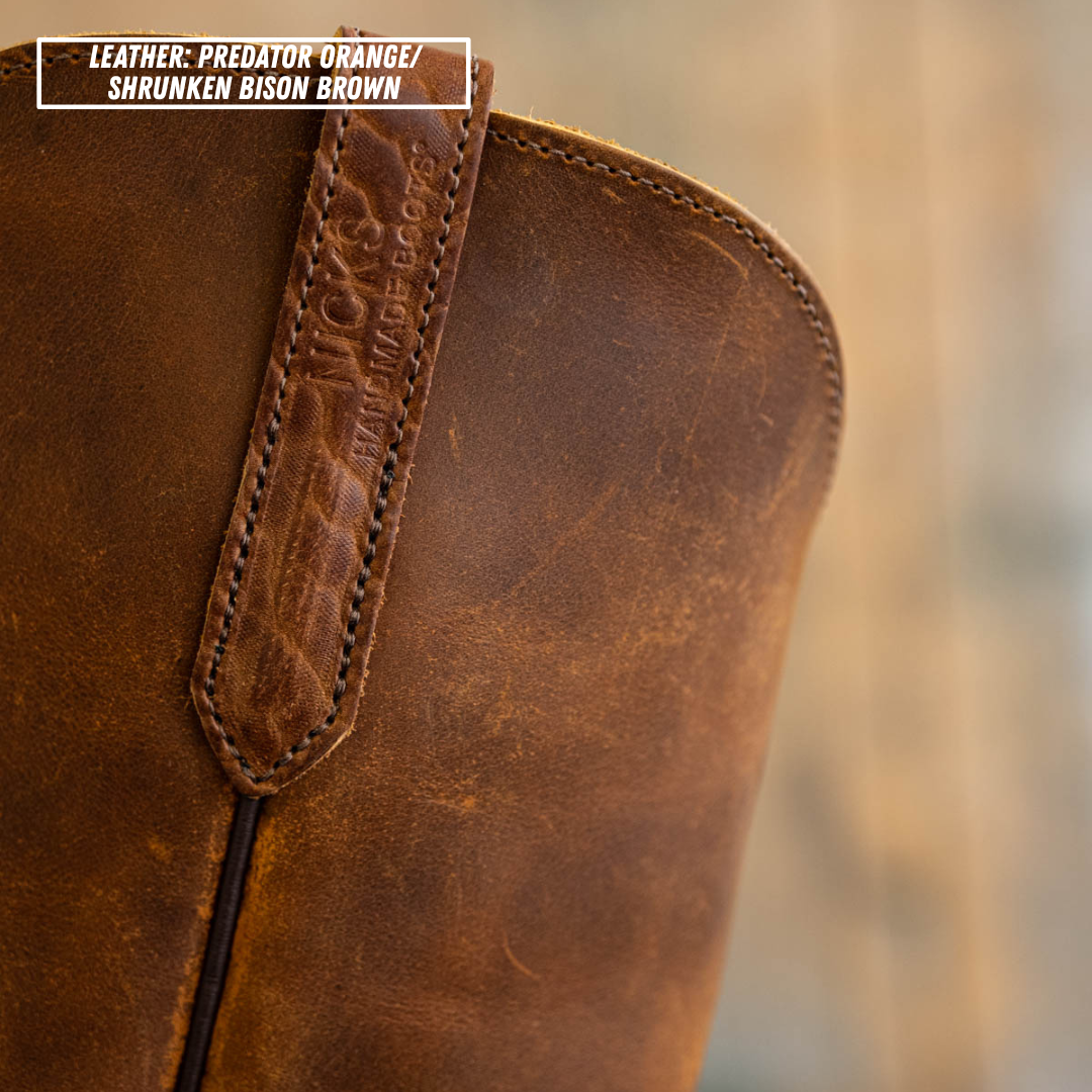 Close-up of a distressed brown leather boot with a pull tab and a text label overlay in the top left corner reading 'LEATHER: PREDATOR ORANGE/ SHRUNKEN BISON BROWN'.