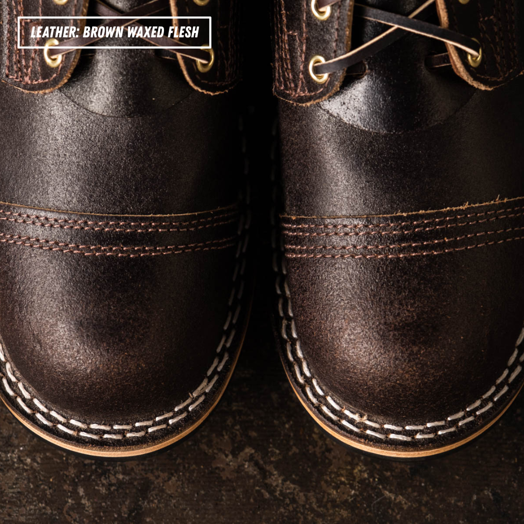 Close-up of a pair of dark brown leather lace-up shoes with white contrast stitching and a textured finish. A text label in the top left reads 'LEATHER: BROWN WAXED FLESH'.