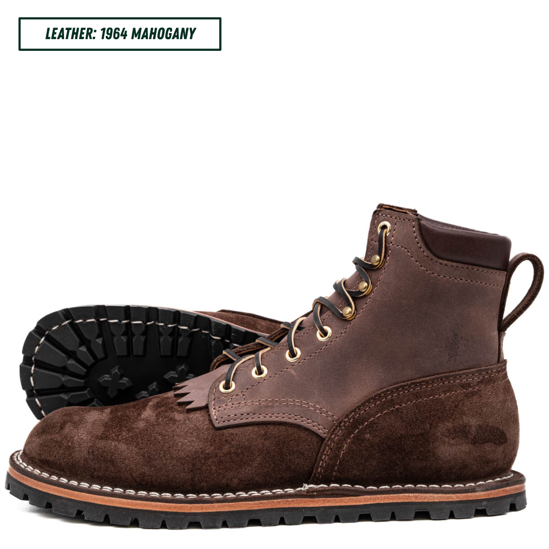 A pair of brown leather lace-up boots, with one boot standing upright and the other lying on its side to show the treaded outsole. The boots feature gold-tone eyelets, a pull tab, and contrast stitching.