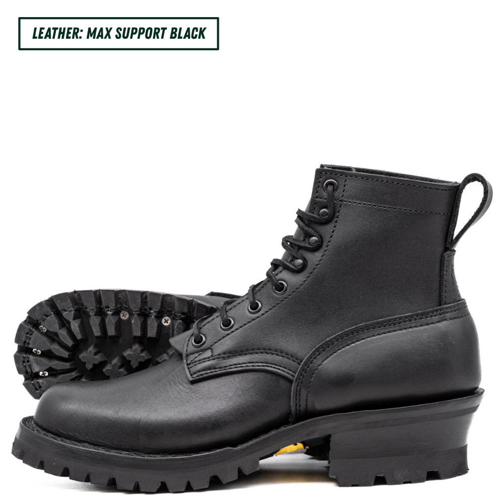 A pair of black leather lace-up boots with rugged lug soles, shown on a white background. One boot is positioned upright in profile, and the other lies behind it showing the treaded outsole.
