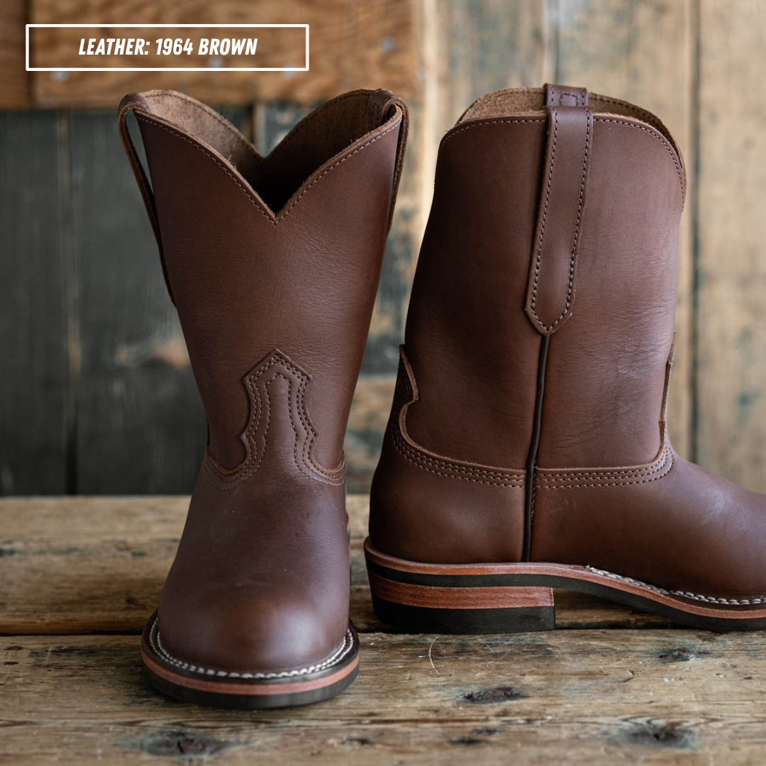 A pair of brown leather cowboy boots displayed on a rustic wooden surface with a wooden plank background. One boot is shown from the front and the other from the side/back.