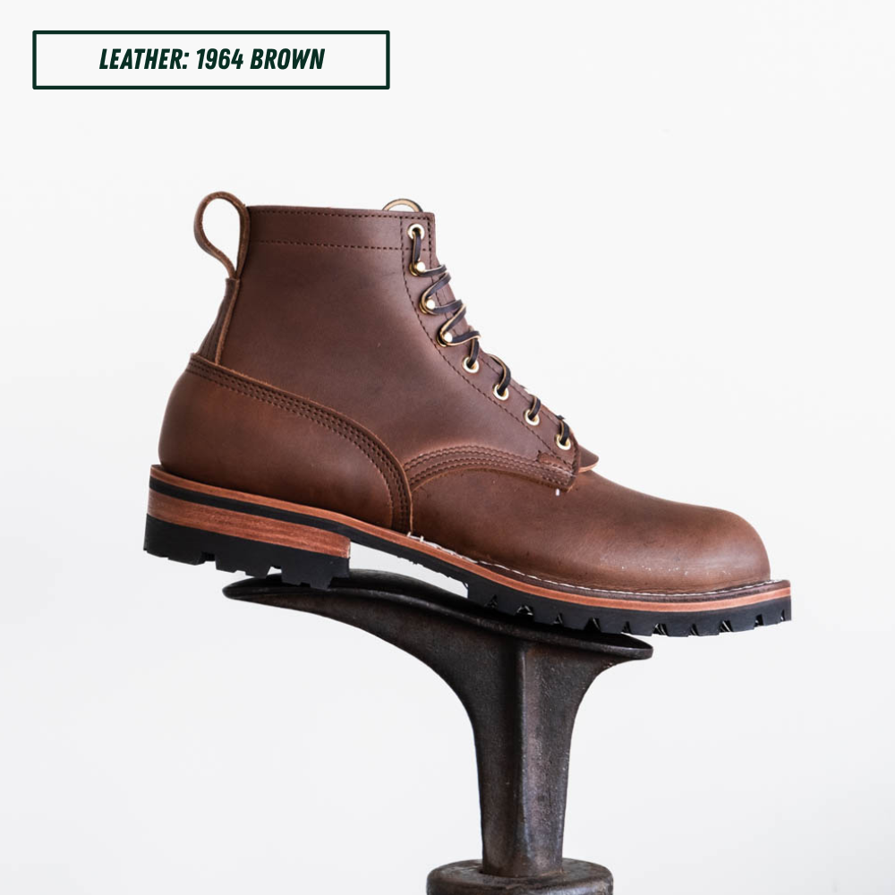 A brown leather lace-up ankle boot displayed on a dark metal stand against a white background, with a text label in the top-left corner reading 'LEATHER: 1964 BROWN'.