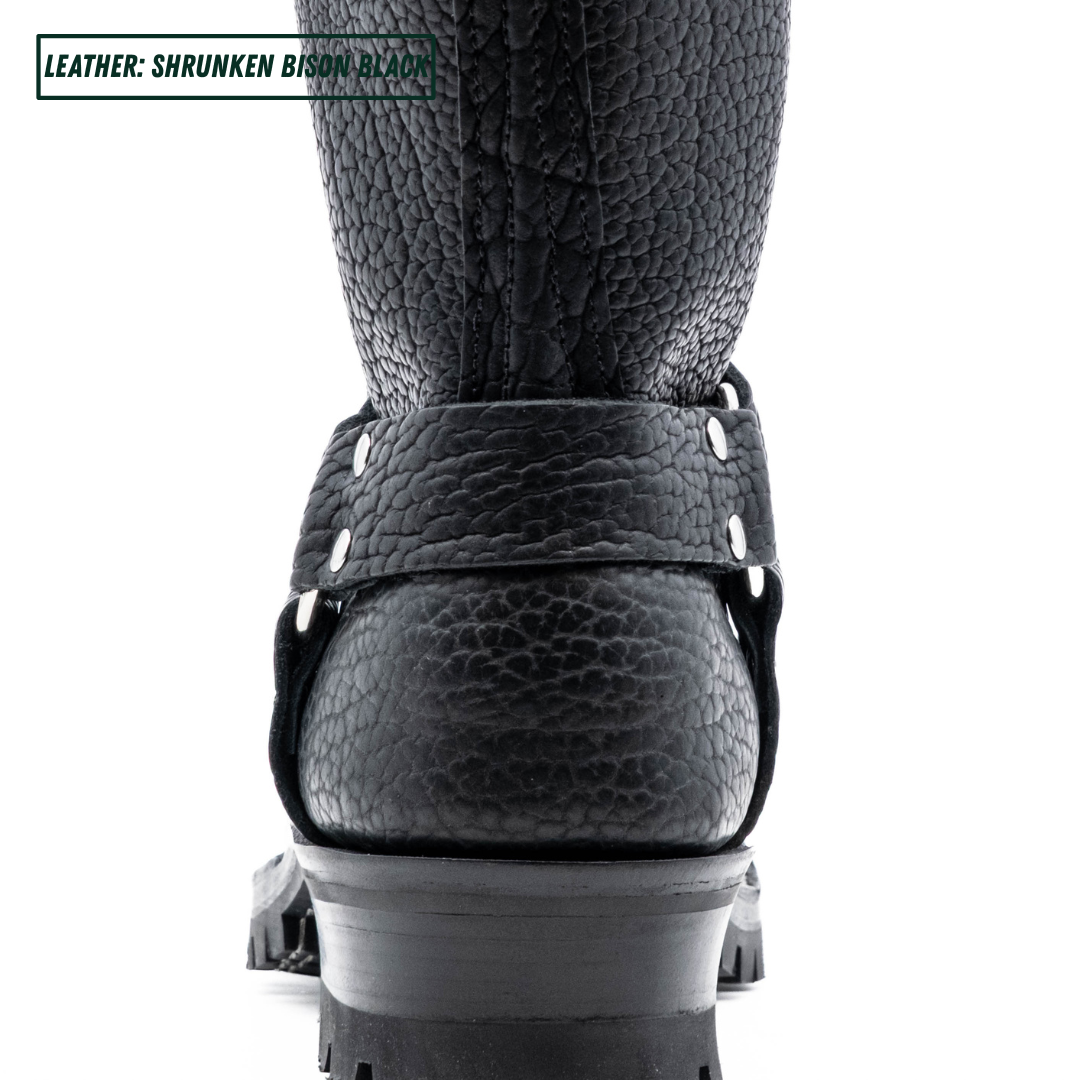 Close-up of the back heel of a black textured leather boot with a thick lug sole and metal rivet details, on a white background with a text label in the top-left corner.