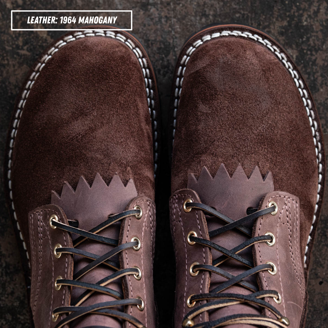 A top-down view of a pair of brown suede and leather lace-up boots on a dark textured background, with a text label in the top-left corner reading 'LEATHER: 1964 MAHOGANY'.