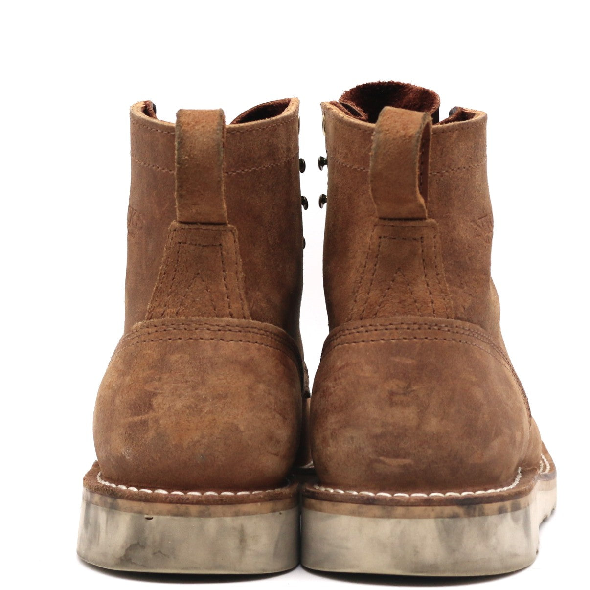A pair of brown suede ankle boots with metal eyelets and thick gray soles, shown from the back against a white background.
