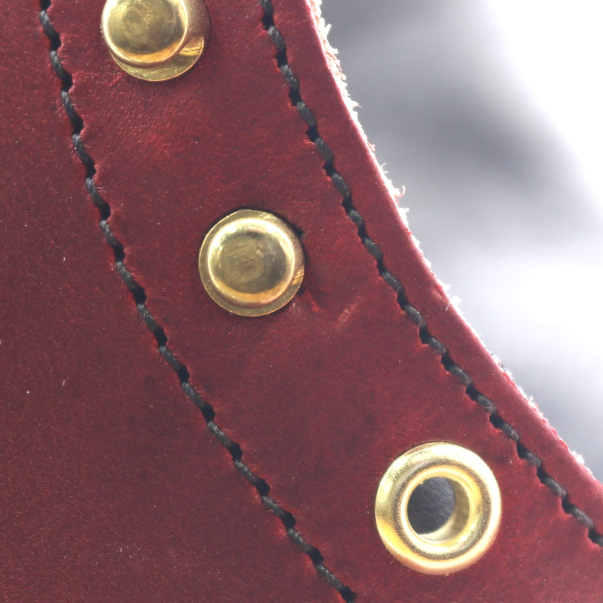 Close-up of a dark red leather strap with black stitching and three brass grommets.