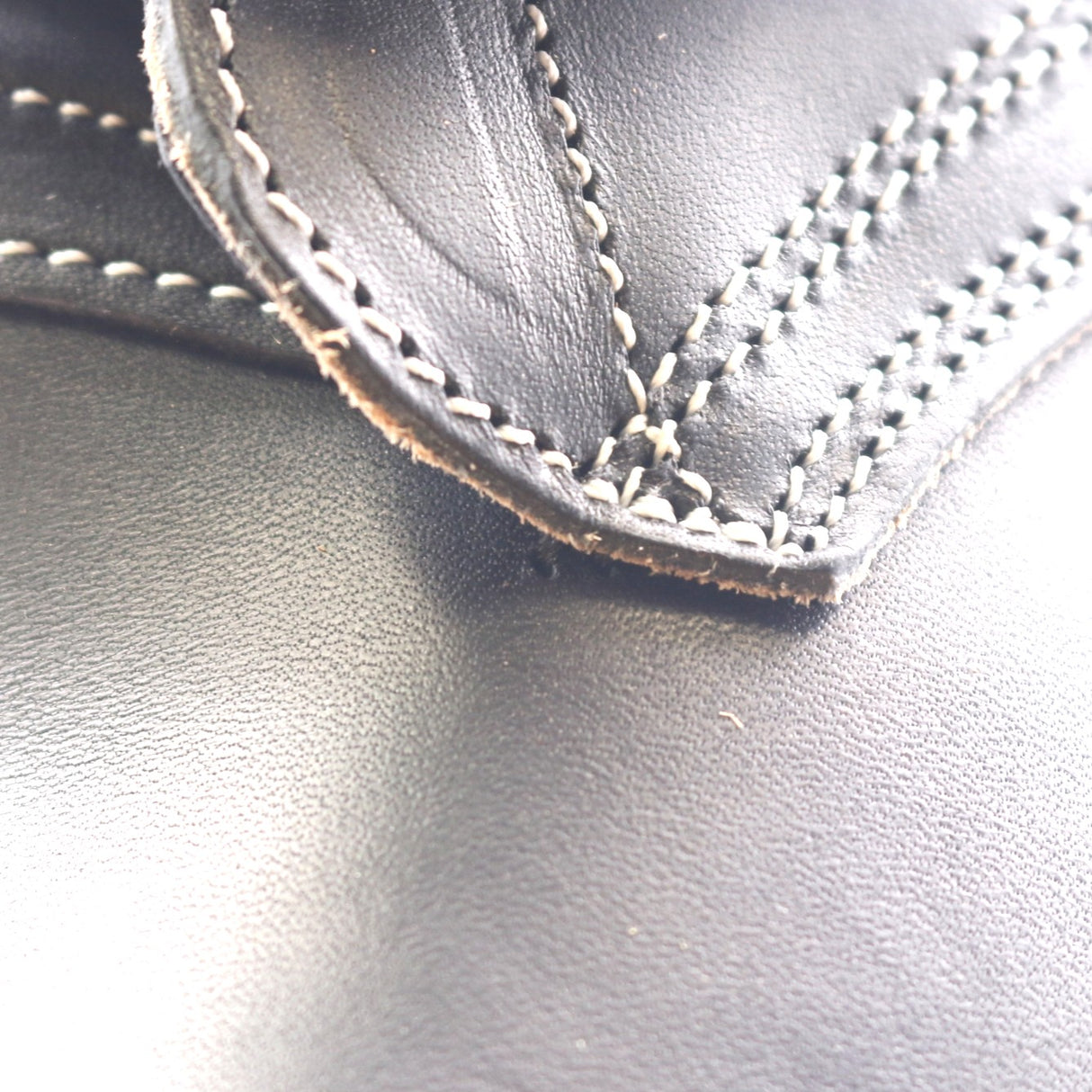 Close-up of black leather with white contrast stitching along a folded edge, showing the texture and construction detail.