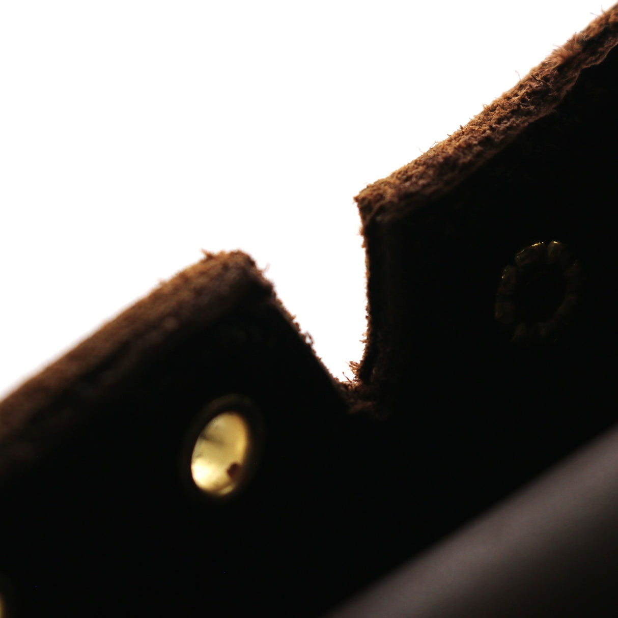 Close-up detail of a dark brown textured leather or felt item with brass-tone rivets against a bright white background.
