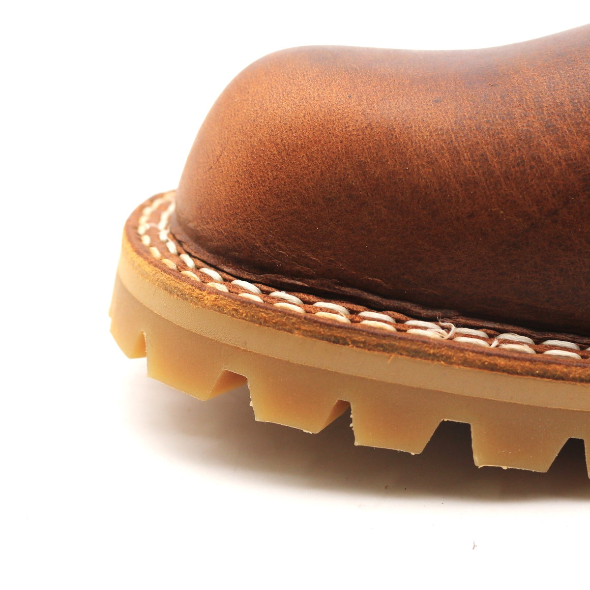 Close-up detail of a brown leather boot corner showing the stacked sole construction with white stitching and a tan rubber outsole on a white background.