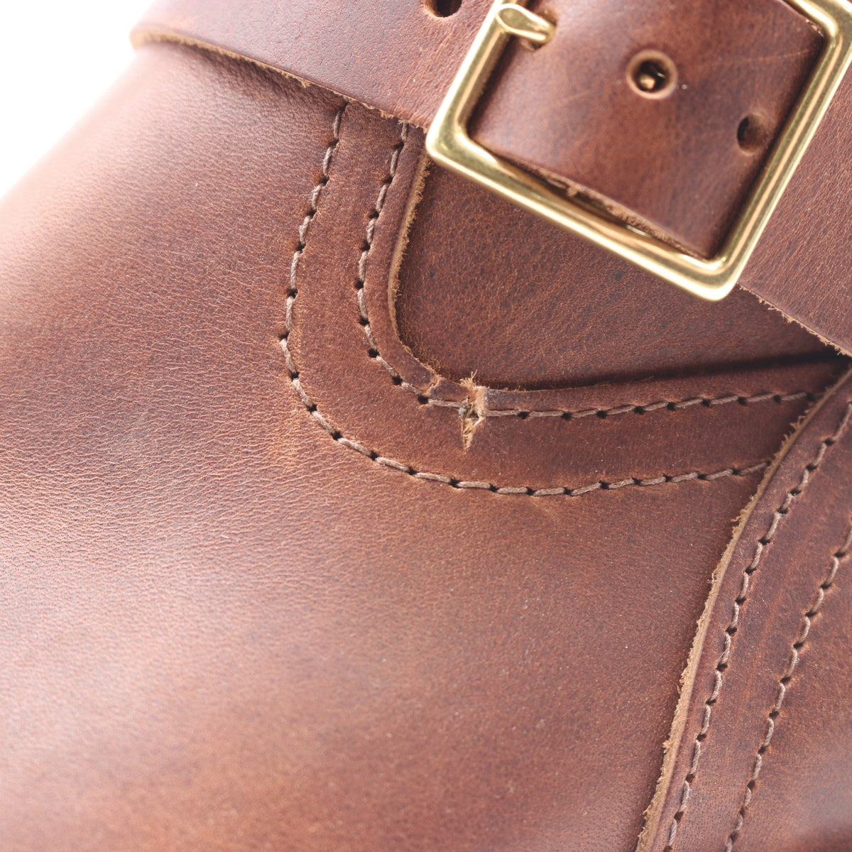 Close-up of a brown leather boot strap with a brass buckle and visible stitching.