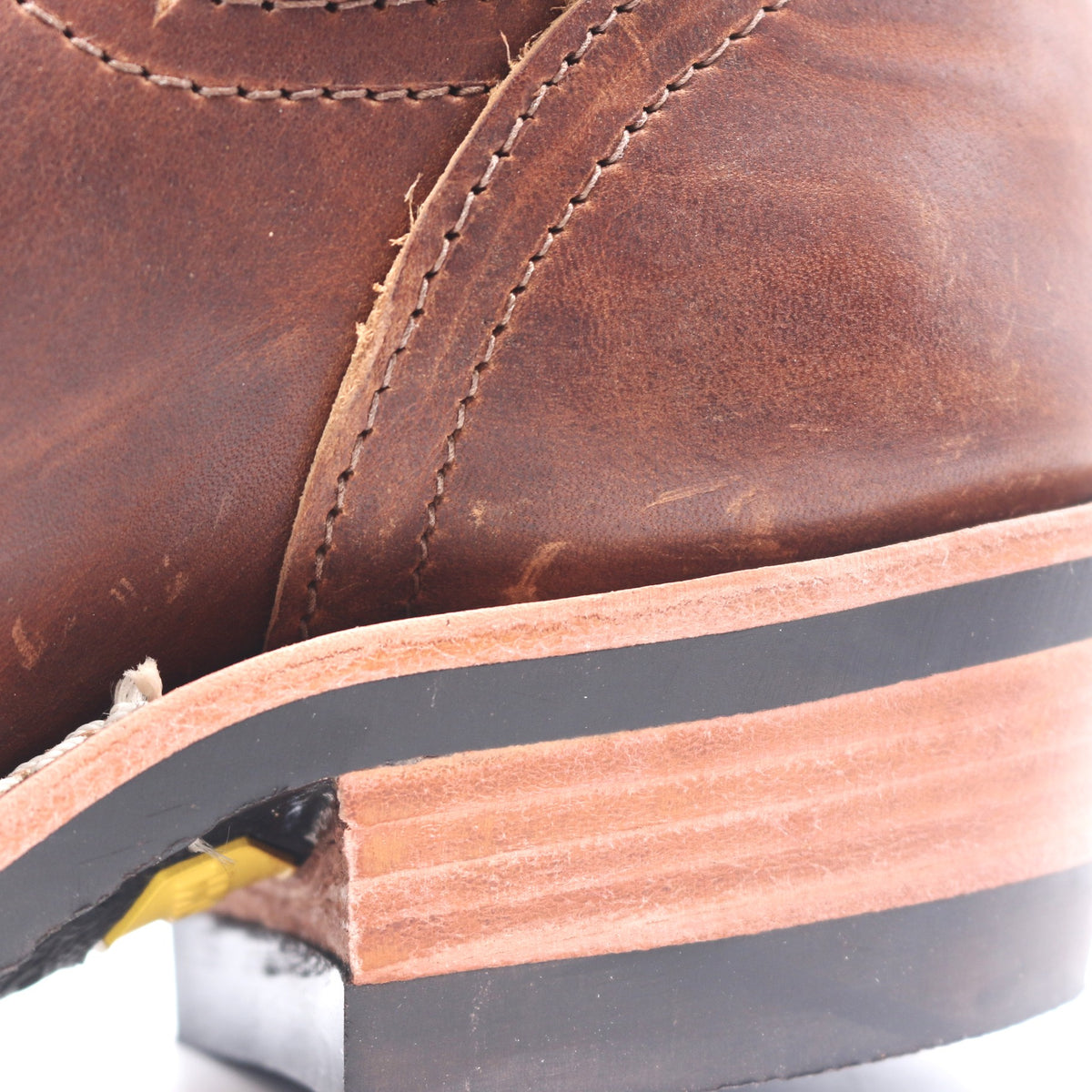 Close-up of a brown leather boot showing the side panel, stitching, and a worn stacked rubber sole with exposed layers.