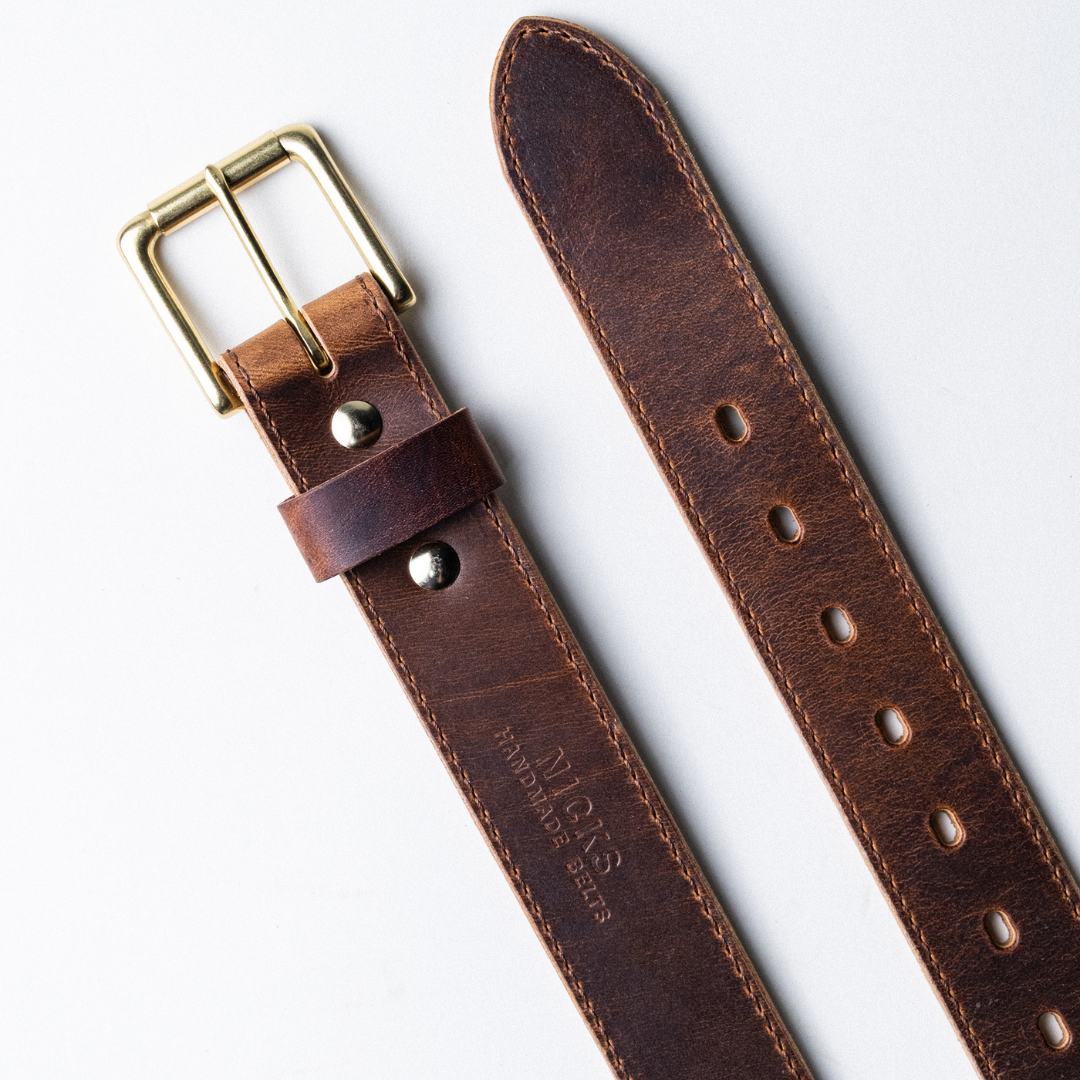 Brown leather belt with gold buckle on a light gray background
