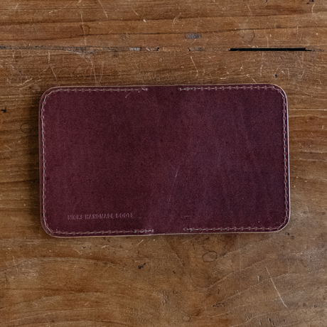 Burgundy leather Heritage Calf Wallet with perimeter stitching lying flat on a wooden surface