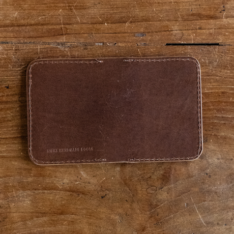 Dark brown leather Heritage Calf Wallet with stitched edges and stamped logo on a wooden background