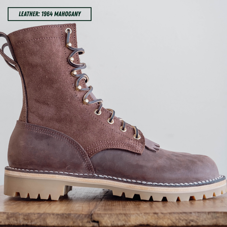 A single lace-up leather boot in a dusty brown shade, shown from a side profile on a wooden surface against a light gray background. A text label in the top left corner reads 'LEATHER: 1964 MAHOGANY'.