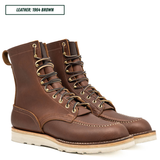 A pair of brown leather lace-up work boots with brass eyelets and a thick white lug sole, shown on a white background with a text label reading 'LEATHER: 1964 BROWN'.