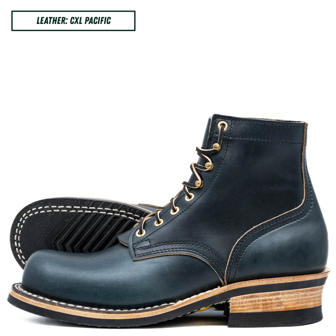 A pair of dark navy blue leather lace-up ankle boots with light tan stitching, gold eyelets, and stacked wood-look heels, shown on a white background with a text label in the top left corner that reads 'LEATHER: CXL PACIFIC'.