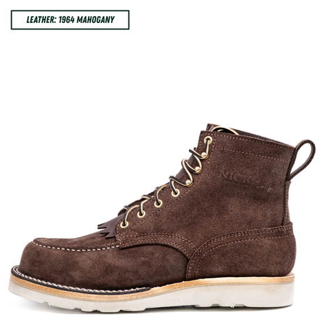 A single brown suede lace-up boot shown in side profile on a white background, with a text label in the top-left corner reading 'LEATHER: 1964 MAHOGANY'. The boot has gold-tone eyelets, white stitching, a light tan midsole, and a white outsole.