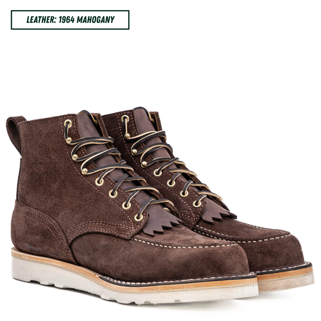 A pair of dark brown suede lace-up boots with fringe detailing on the sides, shown against a white background with a text label in the top left corner that reads 'LEATHER: 1964 MAHOGANY'.