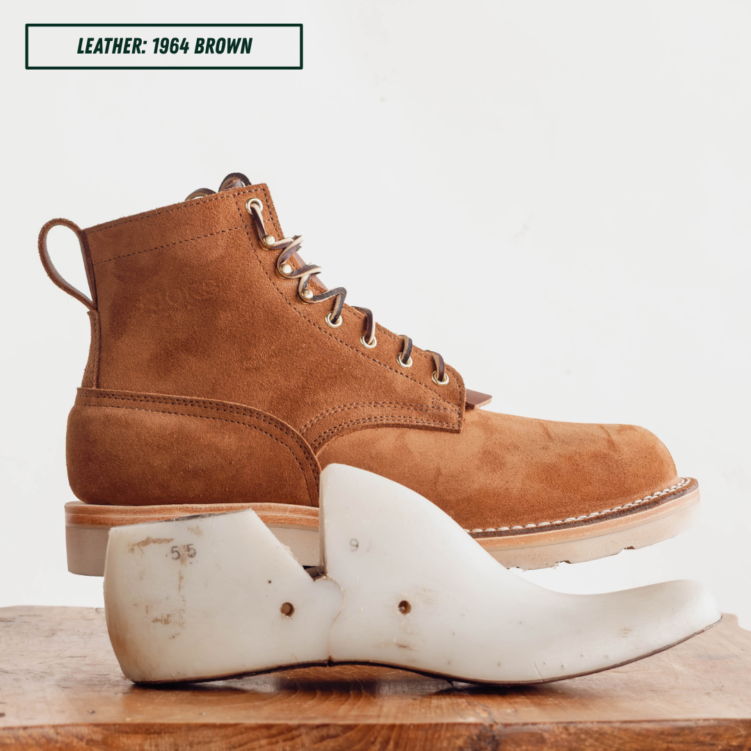 A brown suede lace-up ankle boot shown in side profile on a boot jack, with a 55 last on a wooden surface below and a text label reading 'LEATHER: 1964 BROWN' in the top left.