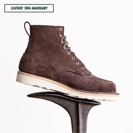 A dark brown suede lace-up ankle boot displayed on a dark metal stand against a white background, with a text label in the top-left corner reading 'LEATHER: 1964 MAHOGANY'.