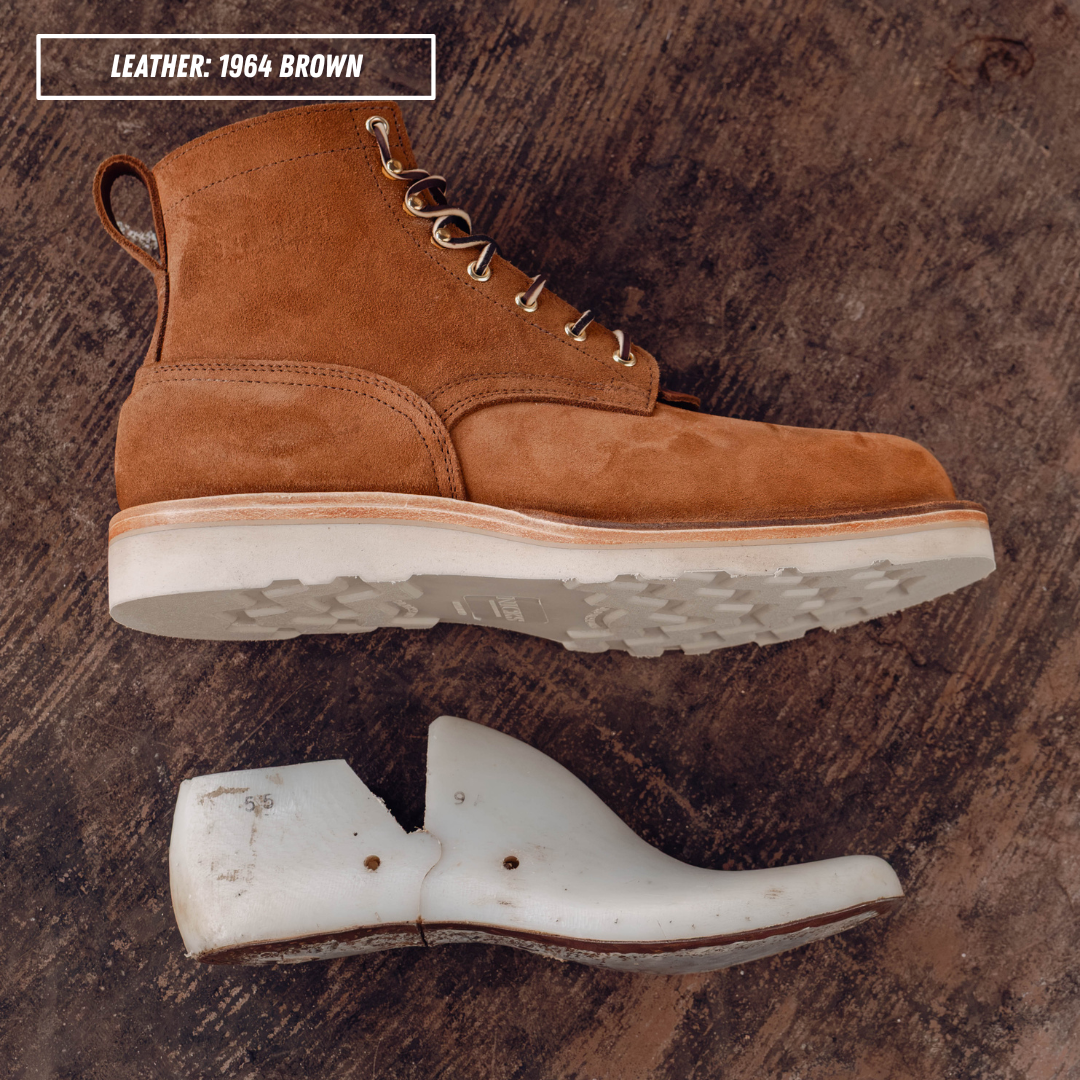 A brown suede lace-up boot shown from side and bottom views on a dark concrete background, with a text label reading 'LEATHER: 1964 BROWN' in the top left corner.