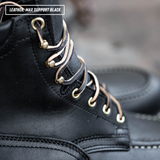 Close-up of a black leather lace-up boot with metallic gold eyelets and laces, featuring a text overlay that reads 'LEATHER- MAX SUPPORT BLACK'.