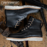 A pair of black leather lace-up boots arranged on a rustic wooden surface with tools in the background. A text box in the top left reads 'LEATHER: MAX SUPPORT BLACK'.