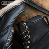 Close-up of black leather lace-up boots with gold-tone eyelets and laces, shown on a rustic wooden surface. A text overlay in the top left reads 'LEATHER: MAX SUPPORT BLACK'.