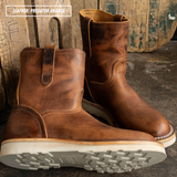 Brown leather pull on boots with white outsole laying on textured concrete and wooden pallet wall in the background.