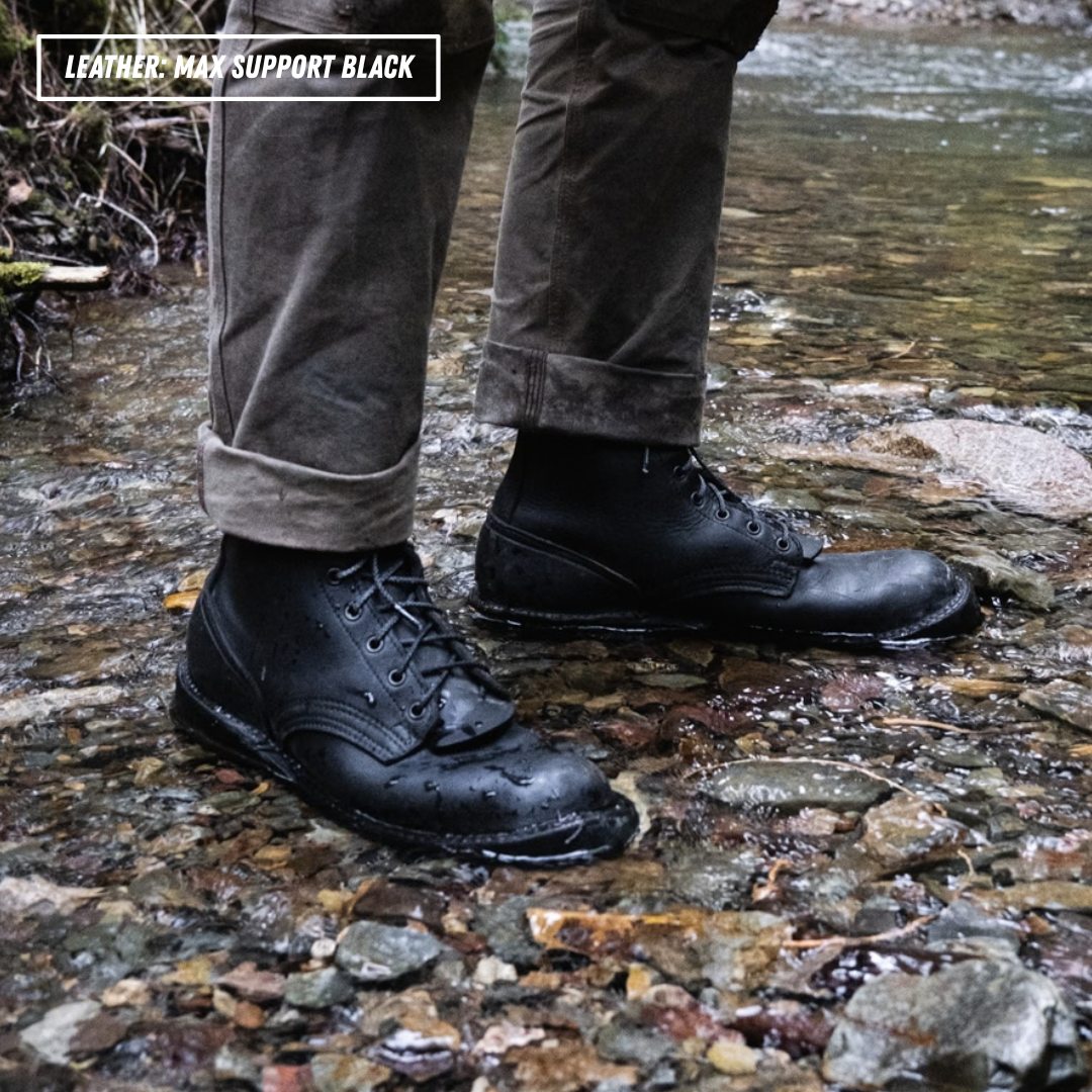 A model wearing black leather boots standing in a creek. Top left reads 'LEATHER: MAX SUPPORT BLACK'