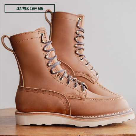 HD moc toe work boots, sitting on wooden table with one propped up. Label on top left of picture that reads "LEATHER: 1964 TAN."