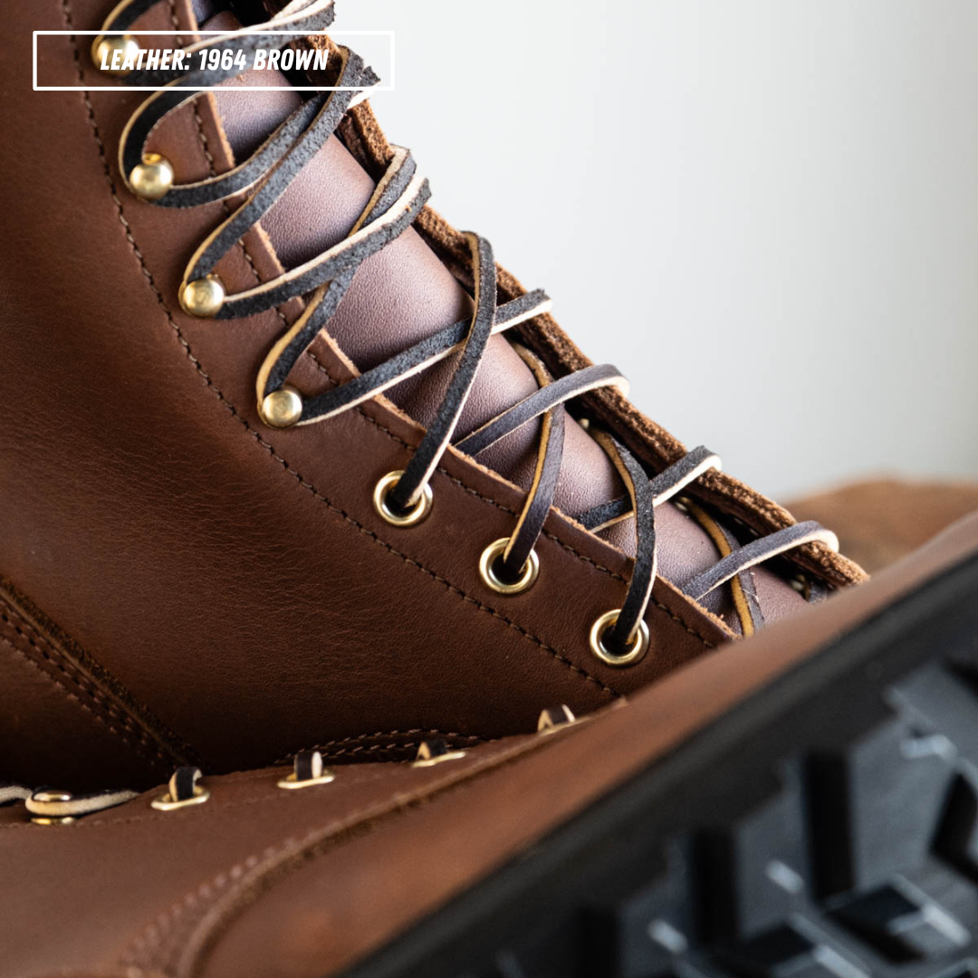 Close-up of a brown leather lace-up boot with dark brown laces threaded through brass eyelets, with a text label reading 'LEATHER: 1964 BROWN' in the top left corner.