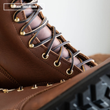 Close-up of a brown leather lace-up boot with dark brown laces threaded through brass eyelets, with a text label reading 'LEATHER: 1964 BROWN' in the top left corner.