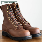 A pair of brown leather lace-up work boots with black laces threaded through brass eyelets, resting on a wooden surface against a plain light background. A text overlay in the top left reads 'LEATHER: 1964 BROWN'.