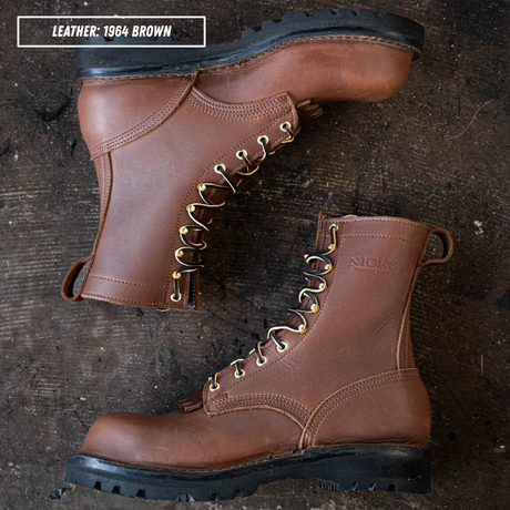 Two brown leather lace-up work boots arranged on a dark rustic wooden surface. One boot is positioned upright and the other lies on its side, showing the side profile and front three-quarter view.