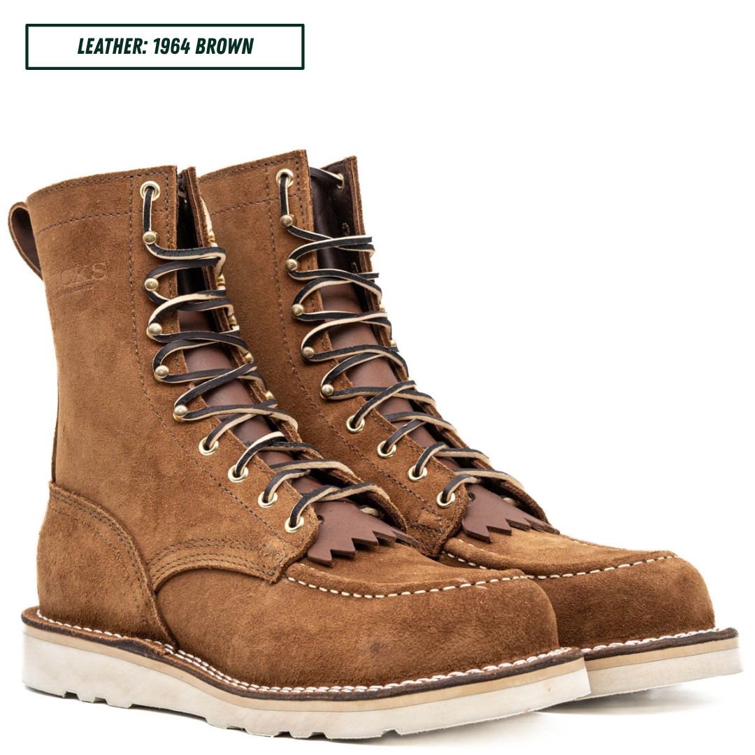A pair of brown leather lace-up work boots with metal eyelets, white stitching, and thick off-white soles, shown on a white background with a text label reading 'LEATHER: 1964 BROWN'.