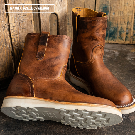 A pair of distressed brown leather mid-calf boots with yellow stitching, shown on a dark rustic surface with wooden planks in the background. A text overlay in the top left reads 'LEATHER: PREDATOR ORANGE'.