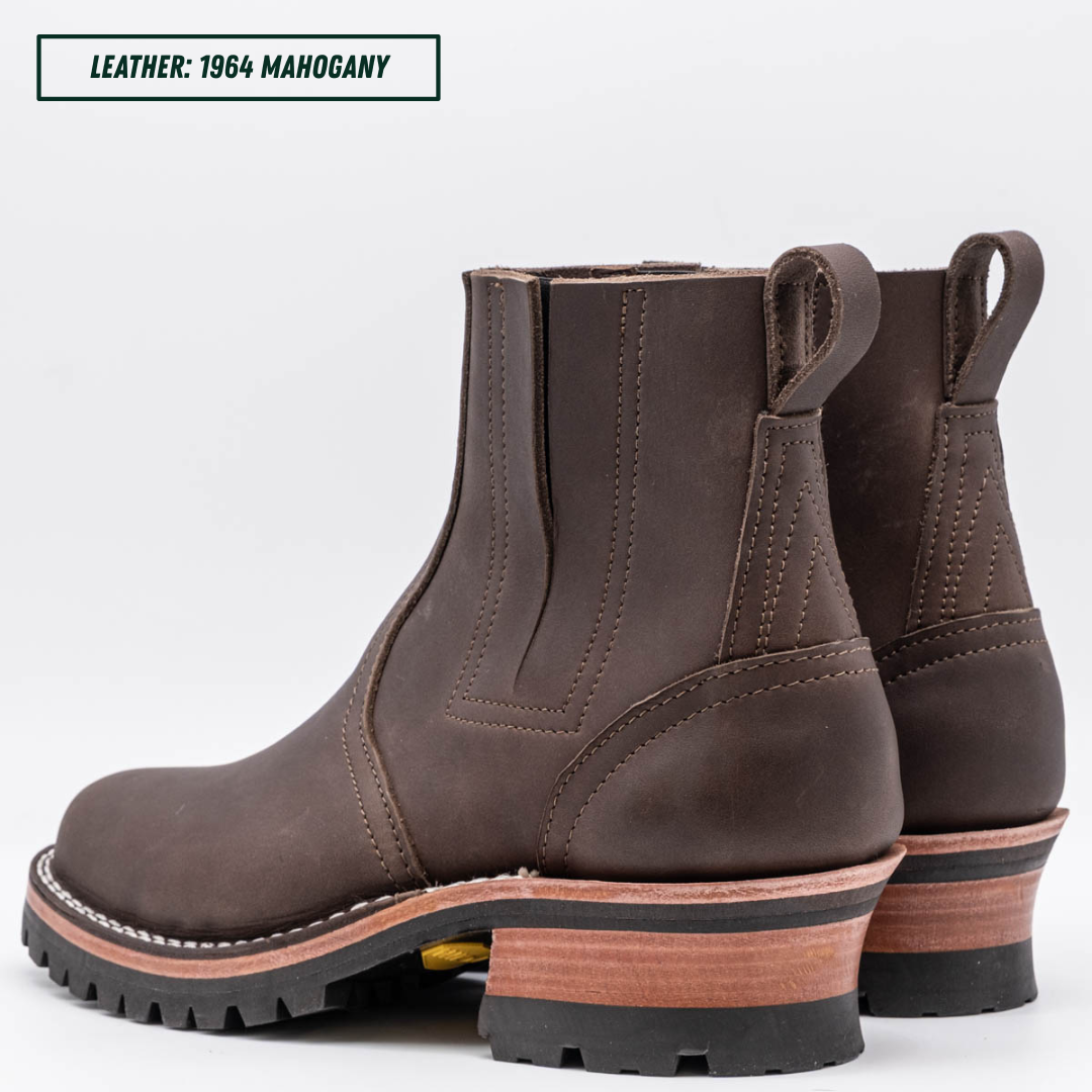 A dark brown leather Chelsea-style ankle boot with a chunky stacked heel, black lug sole, and a light tan midsole section. Boots sitting together facing back left. Top left reads "LEATHER: 1964 MAHOGANY."