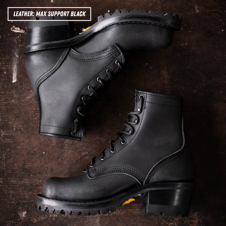 A pair of black leather lace-up boots with rugged lug soles, arranged on a dark rustic wooden surface. A text overlay in the top-left corner reads 'LEATHER - MAX SUPPORT BLACK'.